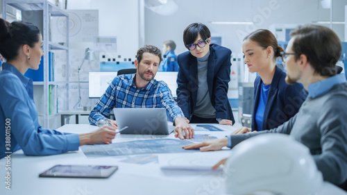 Modern Factory Office Meeting Room: Multi Ethnic and Diverse Team of Engineers, Managers and Investors Talking Sitting at Conference Table, Analyzing Blueprints. High-Tech Manufactory Optimization
