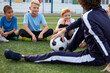 © Roman - friendly kid boys have rest with trainer during football competition, confident male trainer give advice, explain and have talk with sportive boys, in stadium