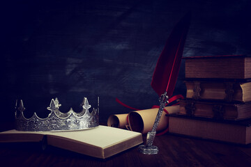 Sticker - low key image of beautiful queen/king crown, old books and feather quill ink pen over wooden table. fantasy medieval period