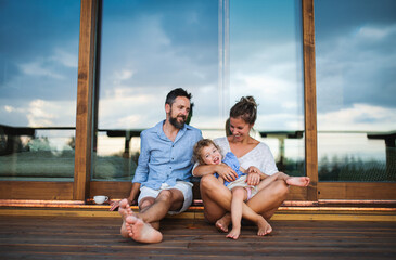 Wall Mural - Family with small daughter sitting on patio of wooden cabin, holiday in nature concept.