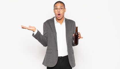 Wall Mural - young black man looking surprised and shocked, with jaw dropped holding an object with an open hand on the side