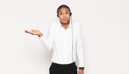 Wall Mural - young black man looking surprised and shocked, with jaw dropped holding an object with an open hand on the side