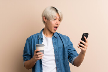 Poster - Young asian man over isolated background holding coffee to take away and a mobile