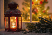 Red Lantern On A Widowsill Covered In Snow On A Snowing Night. A Christmas Tree Inside The House In Visible Through The Window.