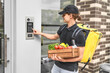 .A man courier with a backpack and vegetables in his hands calls the intercom to deliver the order to the customer online