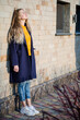 © Iryna - Beautiful young blonde girl in yellow sweater, white sneakers and blue coat, in yellow glasses stay against brick wall