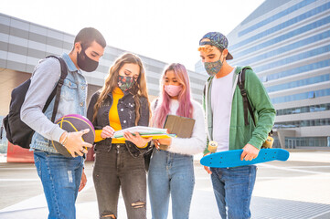 Group of multiracial students in protective masks discuss past lessons outside a college on the street