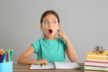 Canvas Print - Emotional little girl doing homework at table on grey background