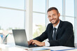 © GVS - Handsome smiling businessman in elegant suit working on laptop in a bright modern office