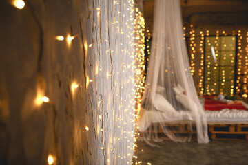 Wall Mural - Christmas decor in the bedroom in the loft style. A four-poster bed made of wooden pallets with white linen and red blankets and pillows. Spruce and gold garlands, illuminated window. New Year.