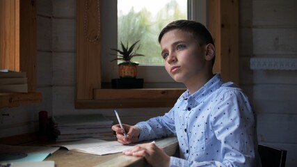 A Beautiful Caucasian Boy in a Blue Shirt is Doing Homework for School