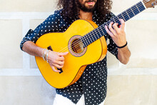 Man Playing Guitar While Standing Against Wall