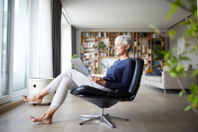 Active Senior Woman Using Laptop While Sitting On Chair At Home