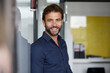 © Rainer Berg/Westend61 - Man smiling while leaning on wall in office
