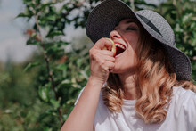 Close-up Of Happy Woman Wearing Hat Eating Apple In Orchard