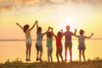 Sticker - Little children jumping near river at sunset, back view