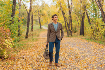 Tall handsome man with a bag on the autumn alley