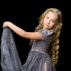 Wall Mural - A little girl in a long, elegant dress of a princess on a black background.