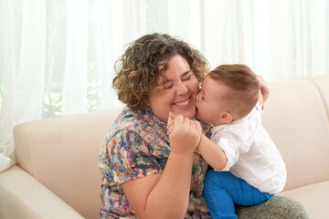 Playful little kid kissing his happy mother on cheek