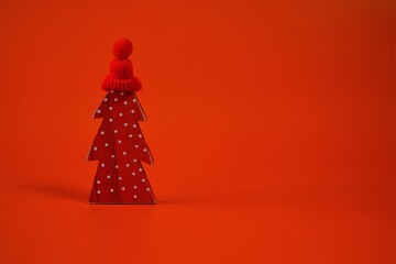 Christmas and New Year festive concept. Red decorative Christmas tree in a red knitted hat on a bright red background. Blank for a Christmas card.Winter holidays background.Festive time.copy space.