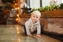 Little Boy In Christmas Loft Bedroom Interior. Christmas Celebration. Infant Boy Weared In Casual. New Year Eve In Loft Room With Red Accents. Lighting Vintage Star On Background