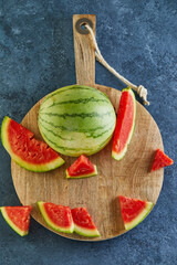 Poster - Mini Watermelon with sliced wedges on a round wooden stand on a blue background