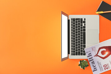 Modern laptop with notebook and magazine on color background