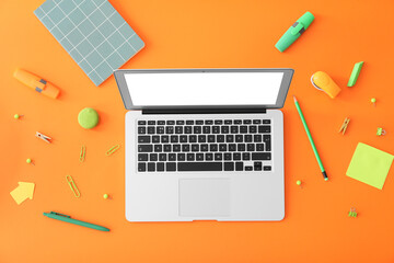 Modern laptop with stationery on color background