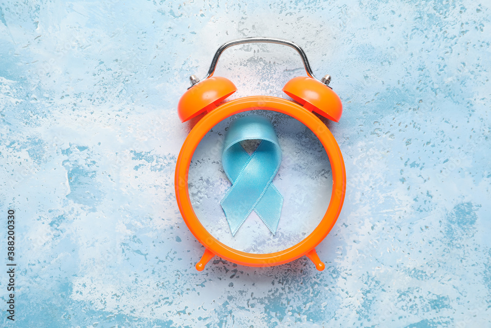 Blue ribbon and alarm clock on color background. Prostate cancer awareness concept
