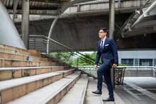 Confidence Asian Businessman Office Worker In Suit Holding Digital Tablet And Walking Up The Stairs At Railway Station In The City. Transportation, Technology And Financial Business Concept.