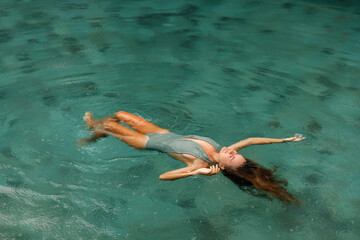 Young woman floating on the back in the simming pool under the rain drops