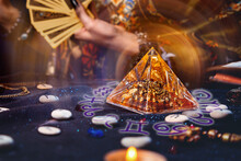Magic Divination And Esotericism. Magic Glass Pyramid With A Magical Glow. In The Background, A Fortune Teller Holds A Fan Of Tarot Cards. Close-up Of Hands