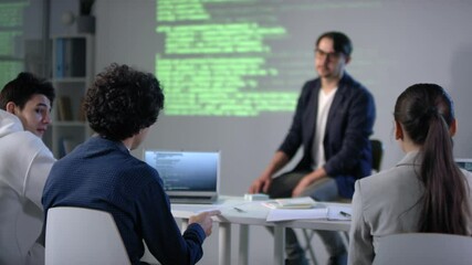 Male pupil raising hand in computer class during IT lesson asking teacher details of computer programming and program coding