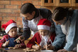 © fizkes - Young Caucasian family with two small kids have fun baking Christmas cookies at home together. Loving parents and little children enjoy decorating cooking biscuits for New Year holiday celebration.