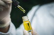 © Tinnakorn - Doctor hand holding bottle of Cannabis oil against Marijuana plant, CBD hemp oil pipette. Cannabis recipe, alternative remedy or medication,  Medical marijuana, medicine concept.