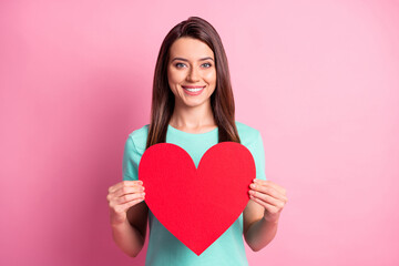 Wall Mural - Photo portrait of beautiful girl keeping red heart shaped card smiling isolated on pastel pink color background