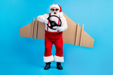 Wall Mural - Full length photo of white grey hair bearded aviator santa claus control steering wheel fly craft wings x-mas eve noel wear red suspenders overalls goggles isolated blue color background