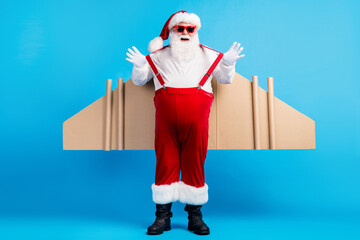 Wall Mural - Full size photo of fat crazy white grey hair bearded santa claus have card board wings pull suspenders x-mas christmas aviator travel wear suspenders overall isolated blue color background