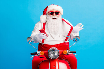 Poster - Photo of grandfather grey beard ride retro scooter play strap hold telephone smile wear santa claus x-mas costume suspenders sunglass white shirt cap gloves isolated blue color background