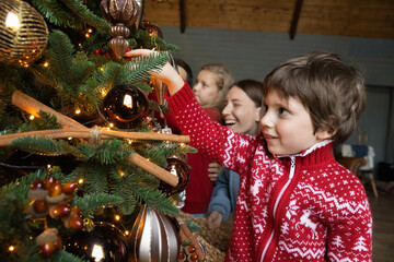 Smiling Caucasian family with small kids celebrate New Year at home decorate Christmas tree together. Happy excited parents and little children have fun with fir-tree decoration on home holidays.