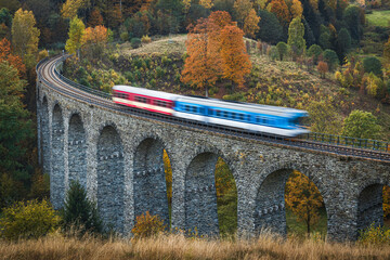  A train going over a beautiful old stone viaduct in autumn colored forest.