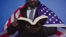 Patriotic Black Man Reading Bible And Holding Flag Of The United States Of America. Close-Up