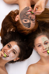 Happy faces of girlfriends with different face masks with cucumbers and a happy smile. Healthy skin, spa concept, vertical close up shot