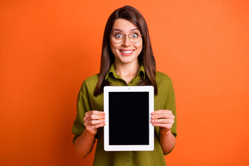 Wall Mural - Photo portrait of amazed female student showing screen empty space on tablet staring in eyewear isolated on vivid orange color background