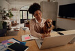 © StratfordProductions - Happy african woman working at home using laptop during quarantine sitting with dog