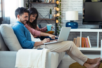 Happy beautiful couple using computer while sitting on the couch at home.