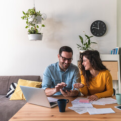 Wall Mural - Smiling couple calculating monthly expenses together at home