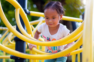 Wall Mural - Asian girl is climbing on a playground equipment in a school.