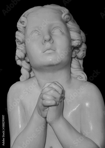 Boy statue pray to God with hands held together. Beautiful old stone statue of praying child isolated on black background