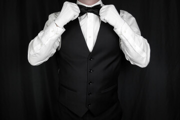 Wall Mural - Portrait of Butler or Waiter in Black Vest and White Gloves Straightening Bow Tie. Concept of Service Industry and Professional Hospitality. Dependable Servant. Copy Space for Service.